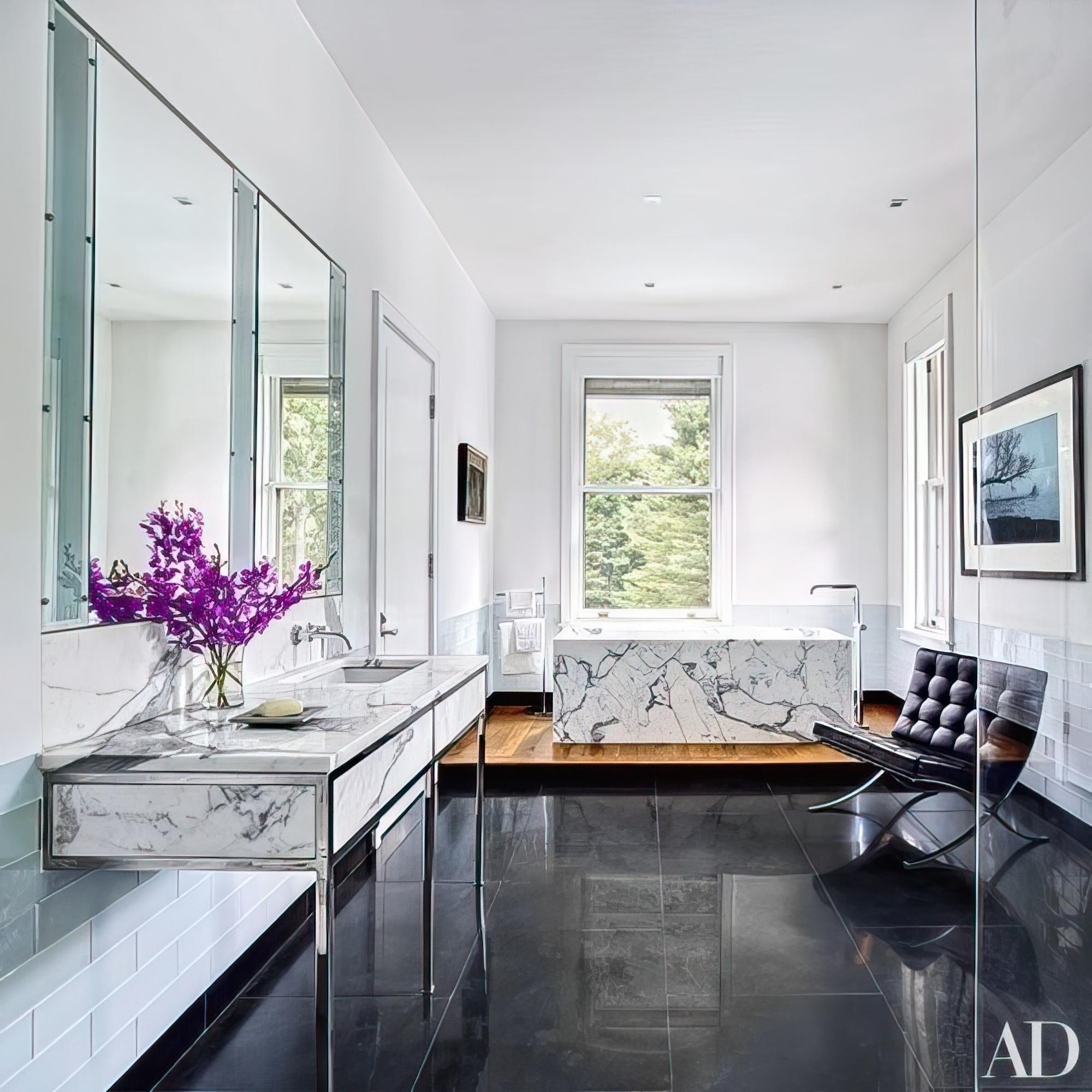 Modern luxury bathroom with marble vanity, freestanding marble bathtub, black tile flooring, and contemporary décor